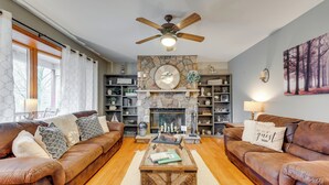 A living room with two brown leather sofas, a wooden coffee table, a stone fireplace, and a ceiling fan. - Pocono Lake House Hideaway: Hot Tub & Theater Room (Pocono Lake)