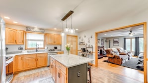 A spacious kitchen with wooden cabinets, a granite countertop, and a central island. There is a dining area with a sofa and a coffee table. - Pocono Lake House Hideaway: Hot Tub & Theater Room (Pocono Lake)