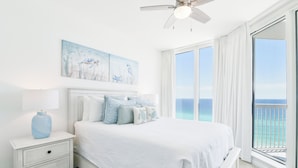 A bedroom with a large bed, a nightstand, a ceiling fan, and a view of the ocean through large windows. - Eleventh Floor Beachfront Condo w/Beach View From Both Bedrooms 🏖️ (Destin)