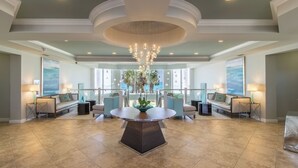A spacious lobby with a central round table, seating area with sofas, and a chandelier. - Eleventh Floor Beachfront Condo w/Beach View From Both Bedrooms 🏖️ (Destin)