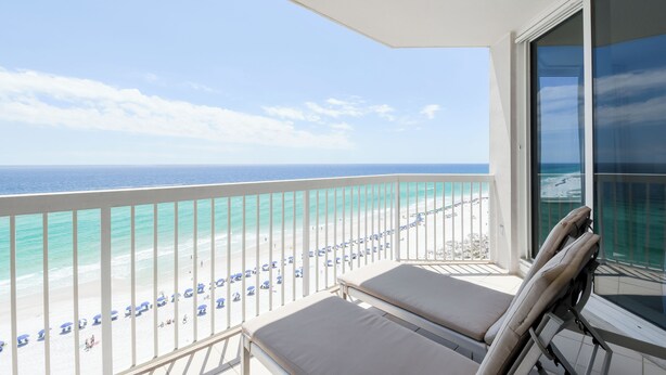 A balcony with two lounge chairs facing a beach with umbrellas. - Eleventh Floor Beachfront Condo w/Beach View From Both Bedrooms 🏖️ (Destin)