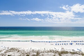Une plage de sable blanc, avec une eau d’un bleu limpide et une rangée de parasols bleus.