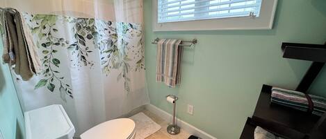 Un baño con inodoro, cortina de ducha estampada con motivos florales, ventana con persianas y toallero con toallas.