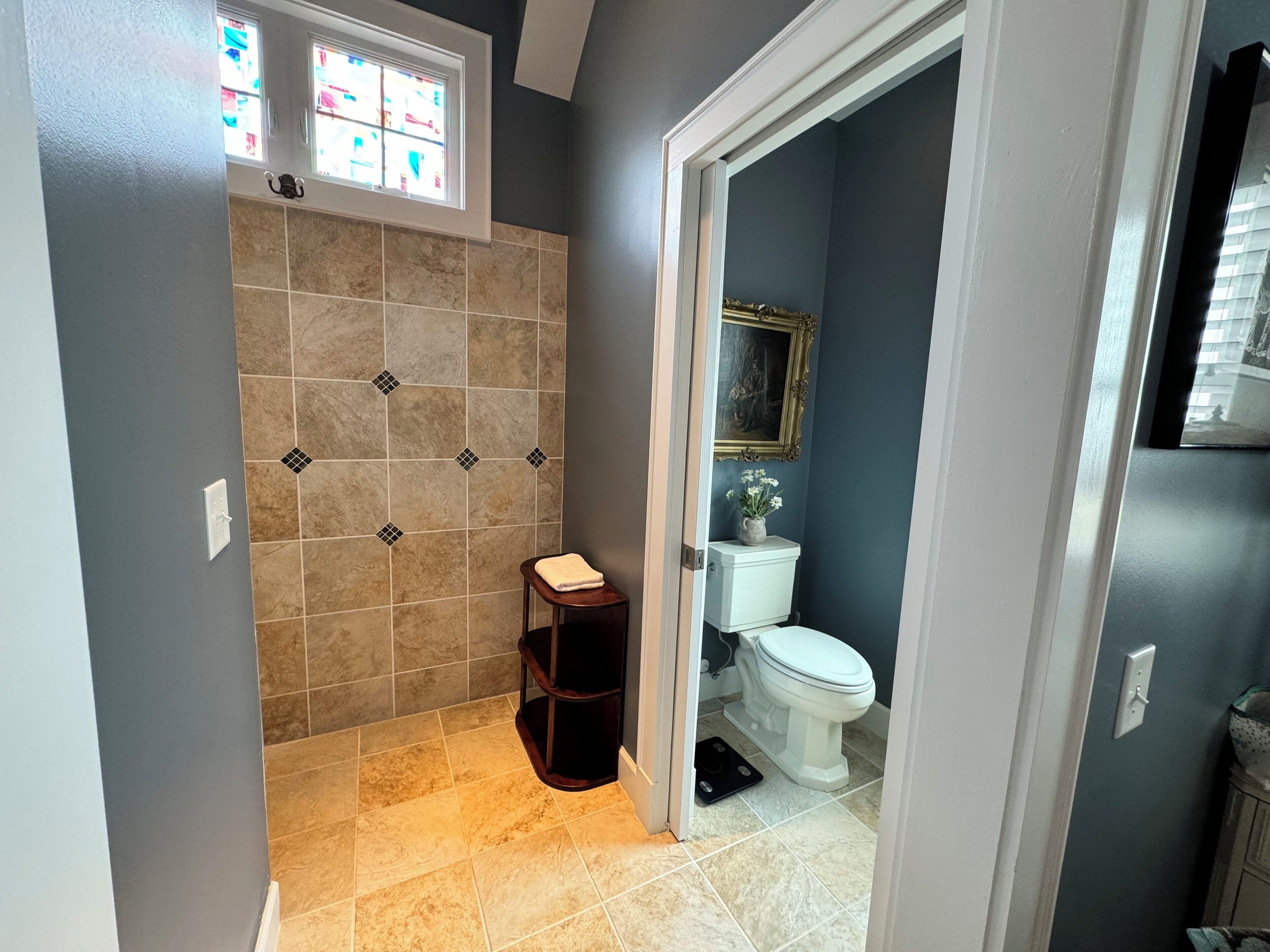 A bathroom with a shower area, a toilet, and a small stool.