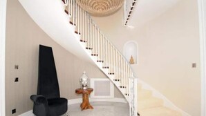Un intérieur moderne avec un escalier à volutes, un fauteuil noir, une petite table d’appoint en bois et un mur blanc.