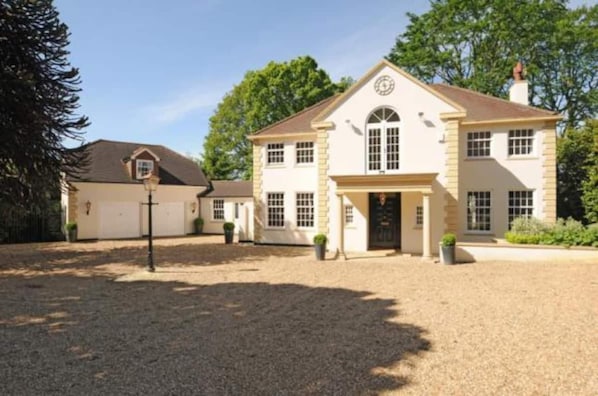 A two-story building with a symmetrical facade, a central entrance with a covered porch, and a clock on the second floor. - Captivating 5-bed House in Woking (Woking)