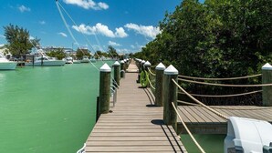 A wooden pier leading to a marina with boats docked on the left. - Seaside Serenity~ Luxury Waterfront Pool Home w/ 35` Dock (Marathon)