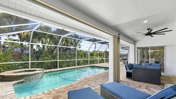A pool area with a glass enclosure, lounge chairs, and a ceiling fan. - 5BR Marco Island Home | Pool & Hot Tub (Marco Island)