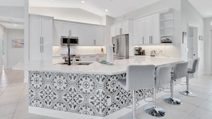A modern kitchen with white cabinetry, stainless steel appliances, and a patterned backsplash. - 5BR Marco Island Home | Pool & Hot Tub (Marco Island)