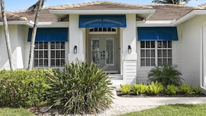 A two-story house with a tiled roof, a front door with a glass panel, and a small front yard with various plants. - 5BR Marco Island Home | Pool & Hot Tub (Marco Island)