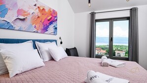 A hotel room with a large bed, a view of the sea, and a colorful abstract painting on the wall. - Luxury Villa Brajdini (Vrbnik)