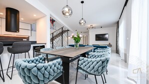 A modern dining area with a wooden table, blue upholstered chairs, and pendant lighting. - Luxury Villa Brajdini (Vrbnik)