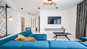 A modern living room with a blue sofa, a black coffee table, and a TV mounted on the wall. - Luxury Villa Brajdini (Vrbnik)