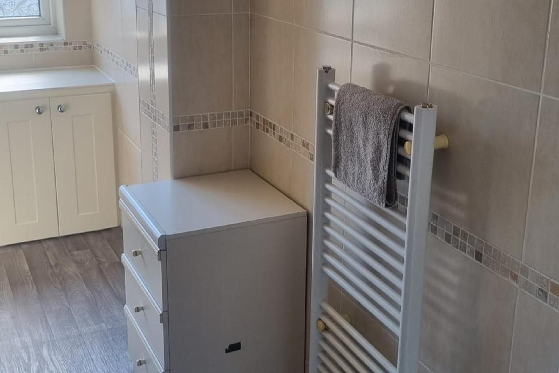 A small, enclosed bathroom with a towel rack, a radiator, and a cabinet.