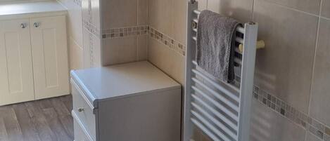 A small, enclosed bathroom with a towel rack, a radiator, and a cabinet.