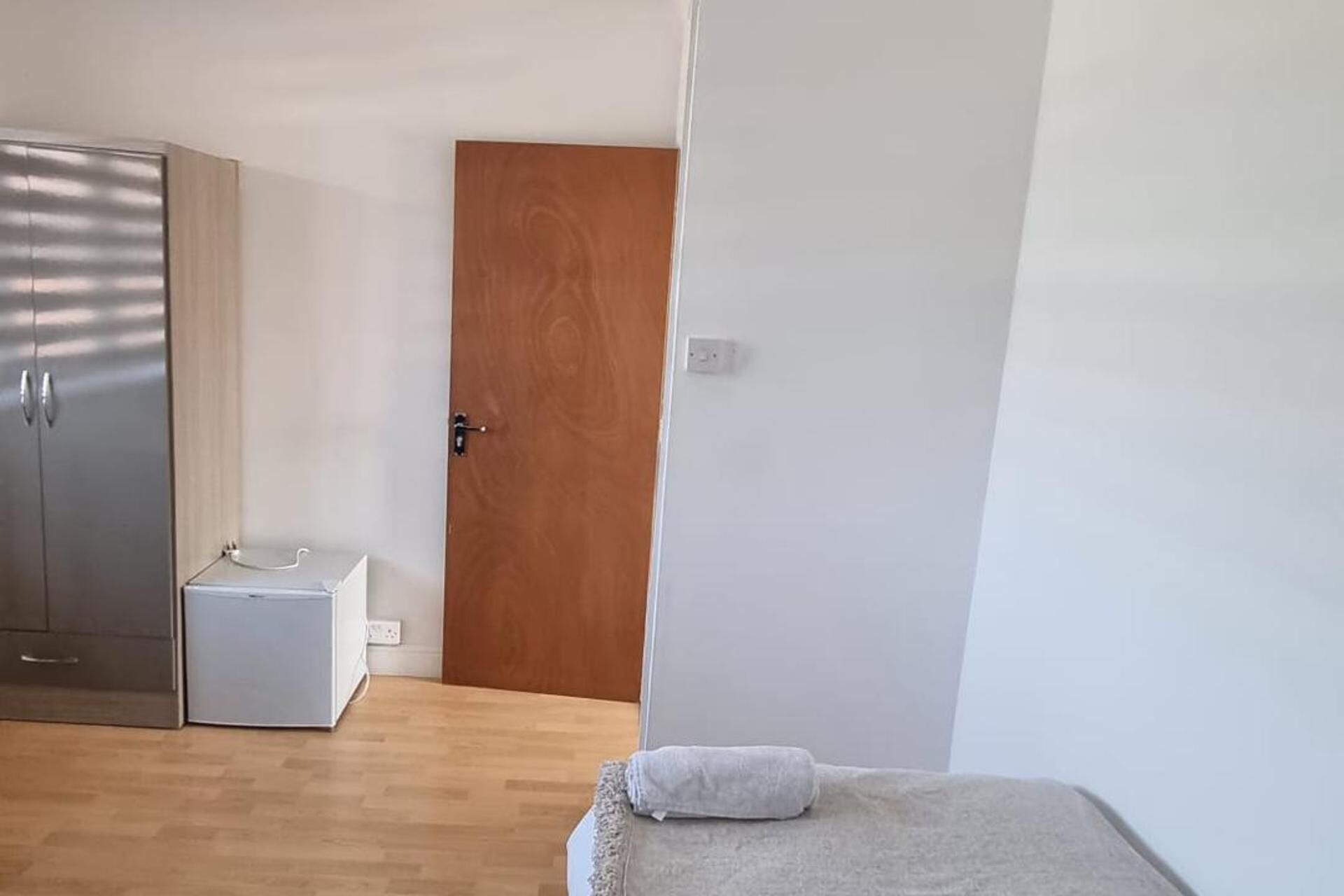 A bedroom with a wooden door, a white bedside table, and a small white object on the table.