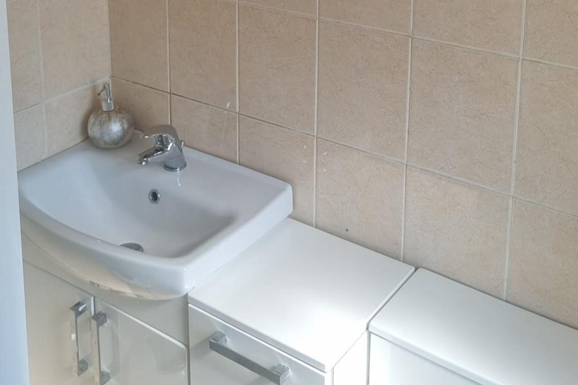 Un baño con lavamanos blanco, un espejo y un armario.