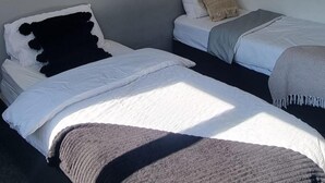 A room with two beds, each with white bedding and a grey blanket. There is a grey wall and a white pillow on one bed. - Doncaster-house-sleeps8-parking-garden (Doncaster)