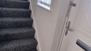 A staircase with carpeted steps leading to a white door with a silver handle and a window above it. - Doncaster-house-sleeps8-parking-garden (Doncaster)