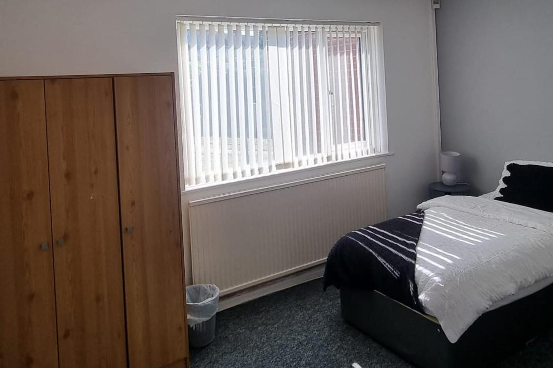 Une chambre à coucher avec un lit, une armoire en bois, un radiateur et une fenêtre avec des stores.