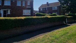 A residential street with two brick houses, a hedge, and a narrow road. - Doncaster-house-sleeps8-parking-garden (Doncaster)