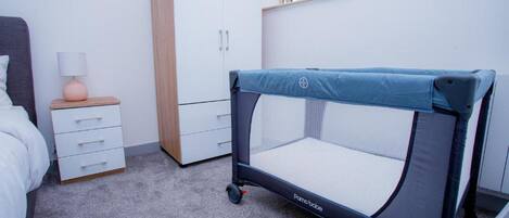 A baby playpen in a bedroom with a bed, dresser, and a window.
