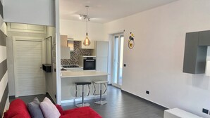 A modern apartment with a red sectional sofa, a kitchen with a tiled backsplash, and a dining area with bar stools. - Casa vacanza a due passi dal mare, centralissima, ristrutturata (Terracina)