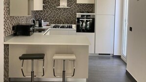 A modern kitchen with a central island, two bar stools, a hanging light fixture, and a tiled backsplash. - Casa vacanza a due passi dal mare, centralissima, ristrutturata (Terracina)