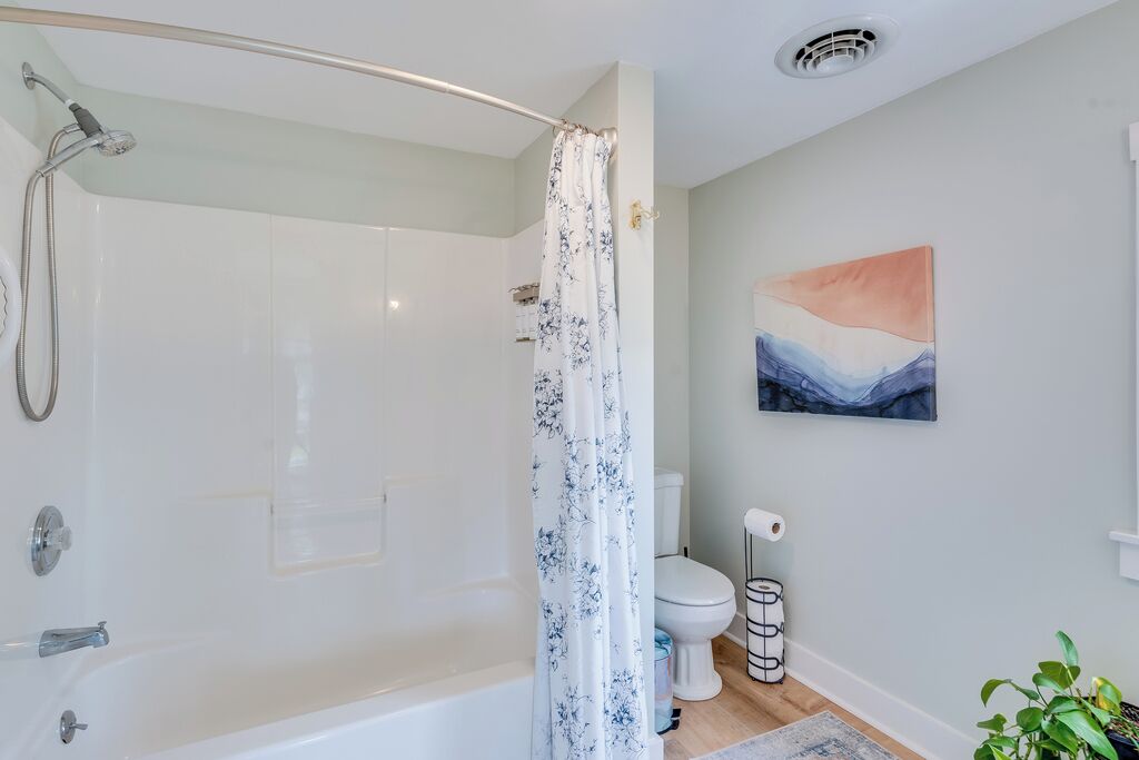 Een badkamer met een bad, douche, toilet en een schilderij aan de muur.
