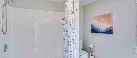 Een badkamer met een bad, douche, toilet en een schilderij aan de muur.