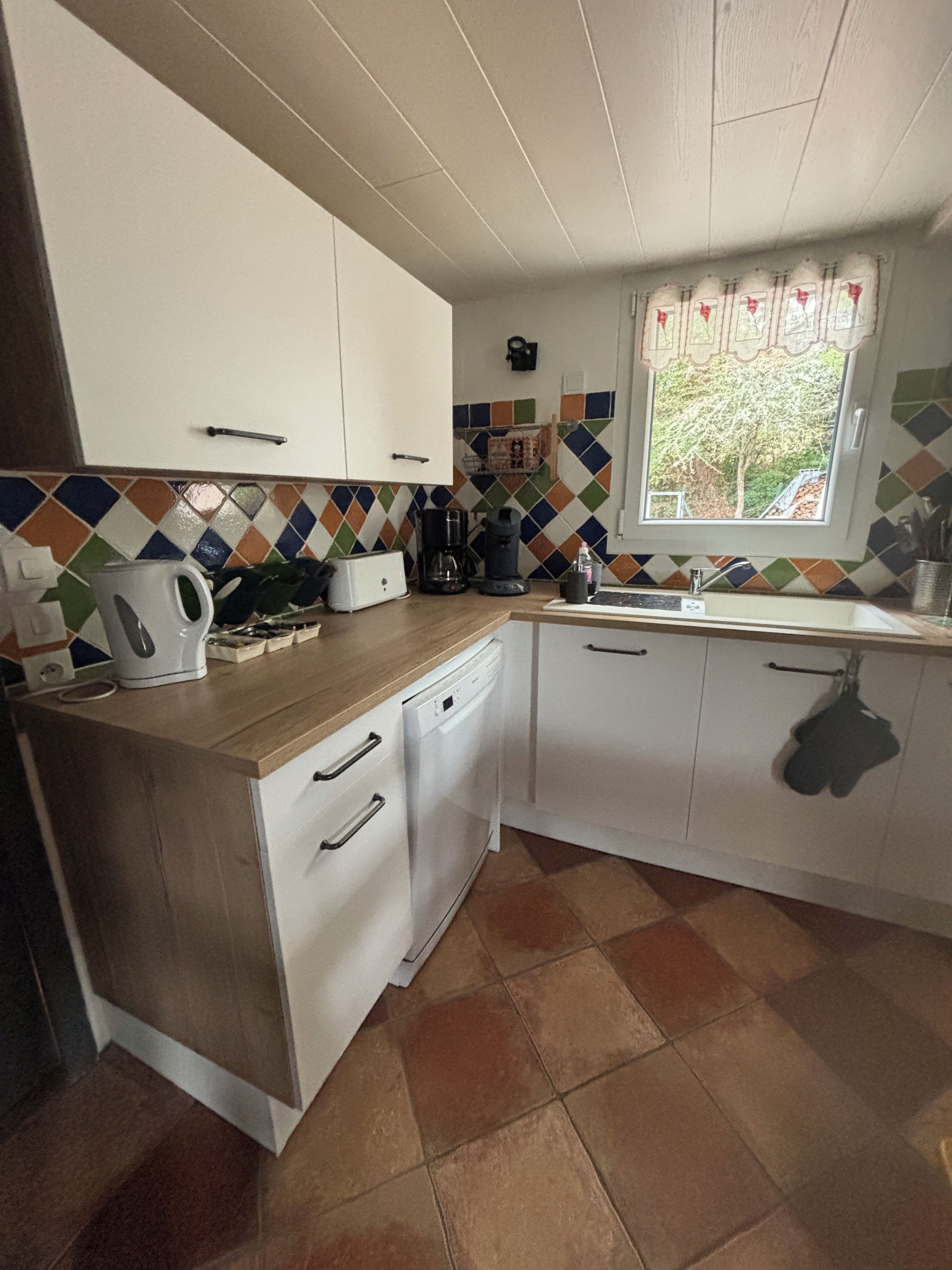 Cozinha com armários brancos, bancada de madeira, cafeteira e janela com vista para árvores.