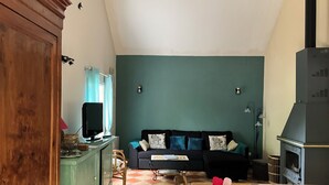 A living room with a green wall, a black sofa, a wooden dining table, and a kitchen area with a stove.