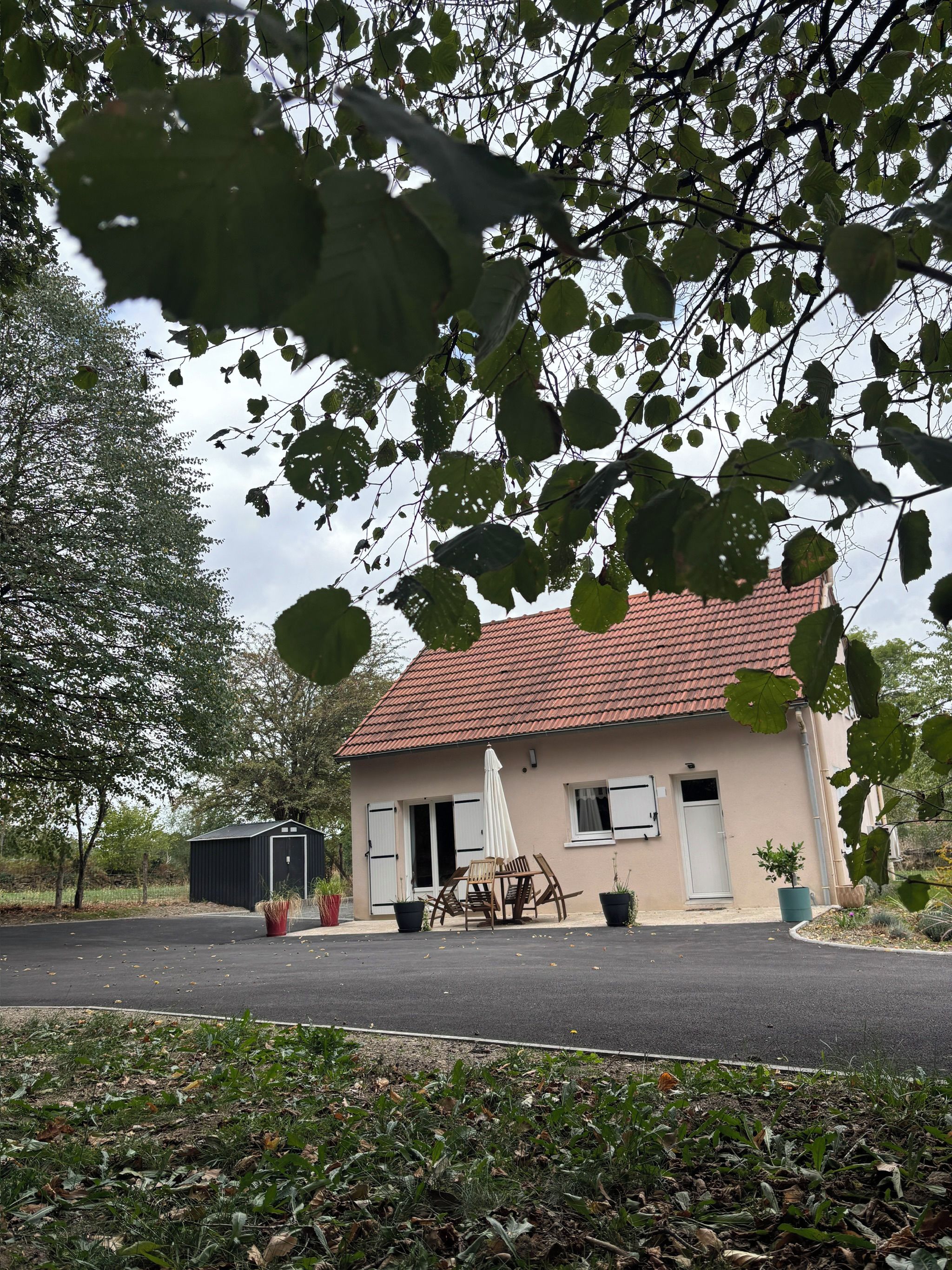Un bâtiment à deux étages, doté d’un toit recouvert de tuiles rouges, d’une petite remise attenante et d’une terrasse aménagée avec du mobilier d’extérieur.