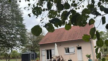 Un bâtiment à deux étages, doté d’un toit recouvert de tuiles rouges, d’une petite remise attenante et d’une terrasse aménagée avec du mobilier d’extérieur.