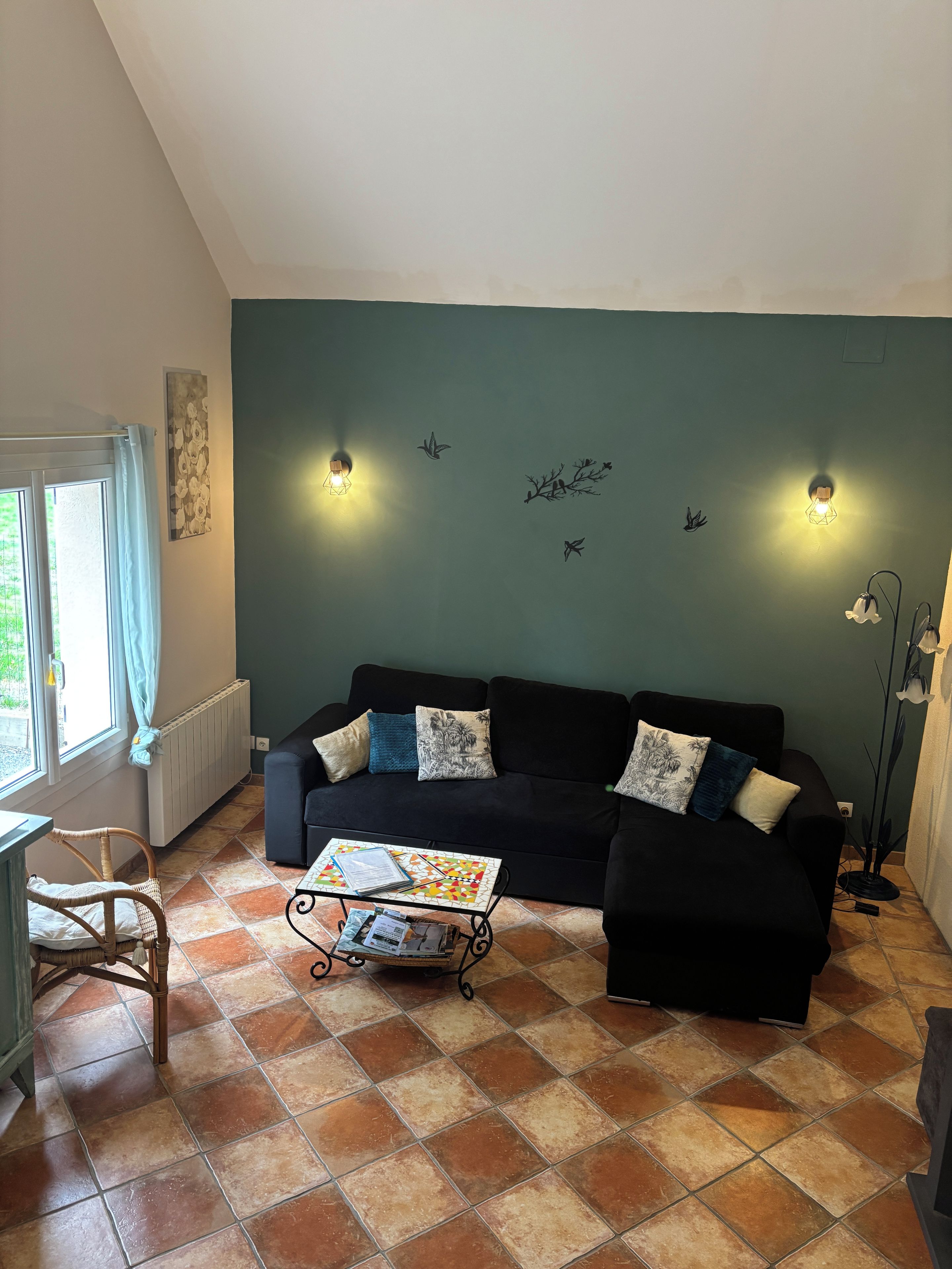 Een woonkamer met een zwarte bank, een klein tafeltje en een raam met gordijnen.
