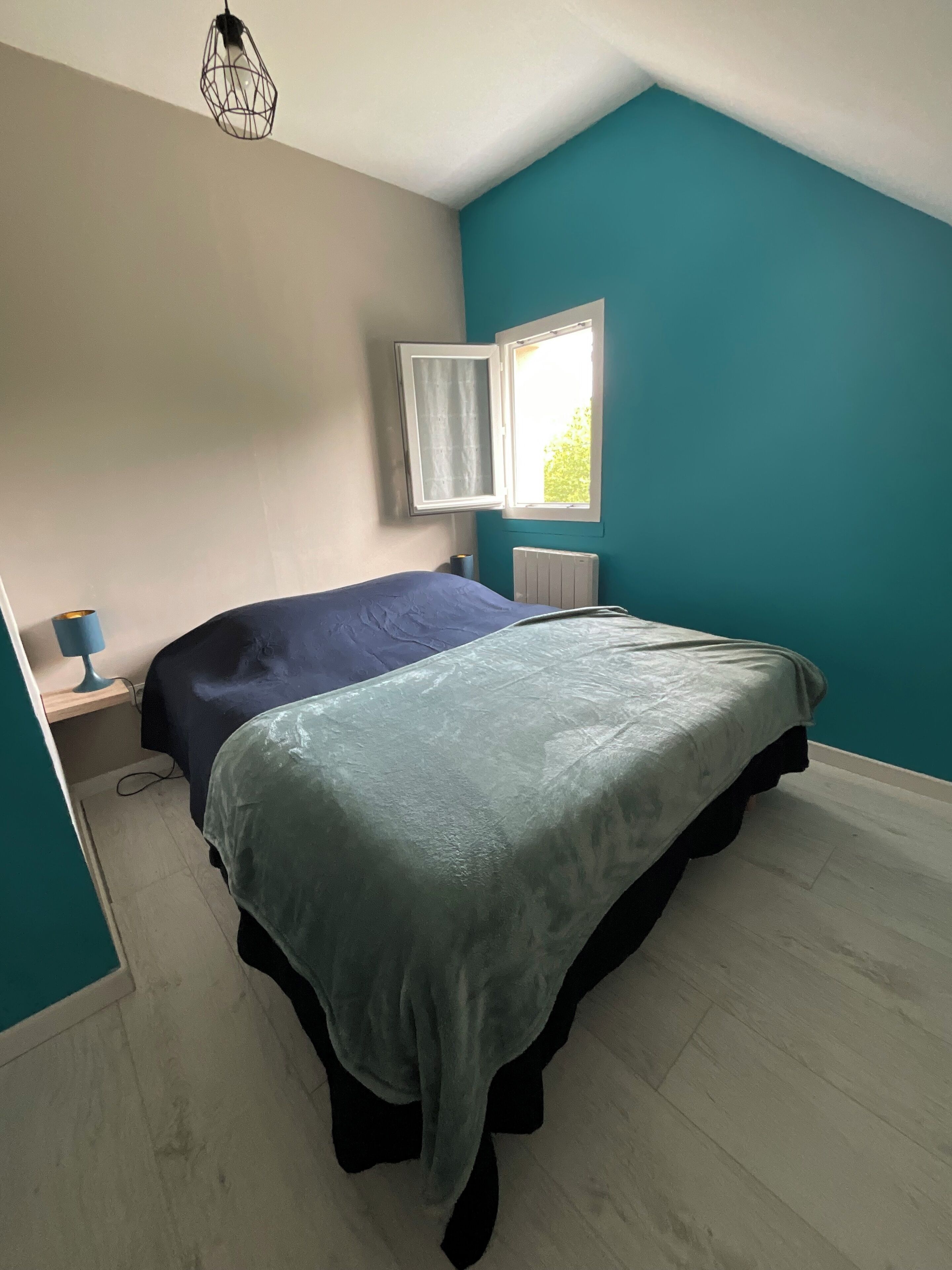 A bedroom with a bed, a nightstand, a lamp, a window, and a radiator.