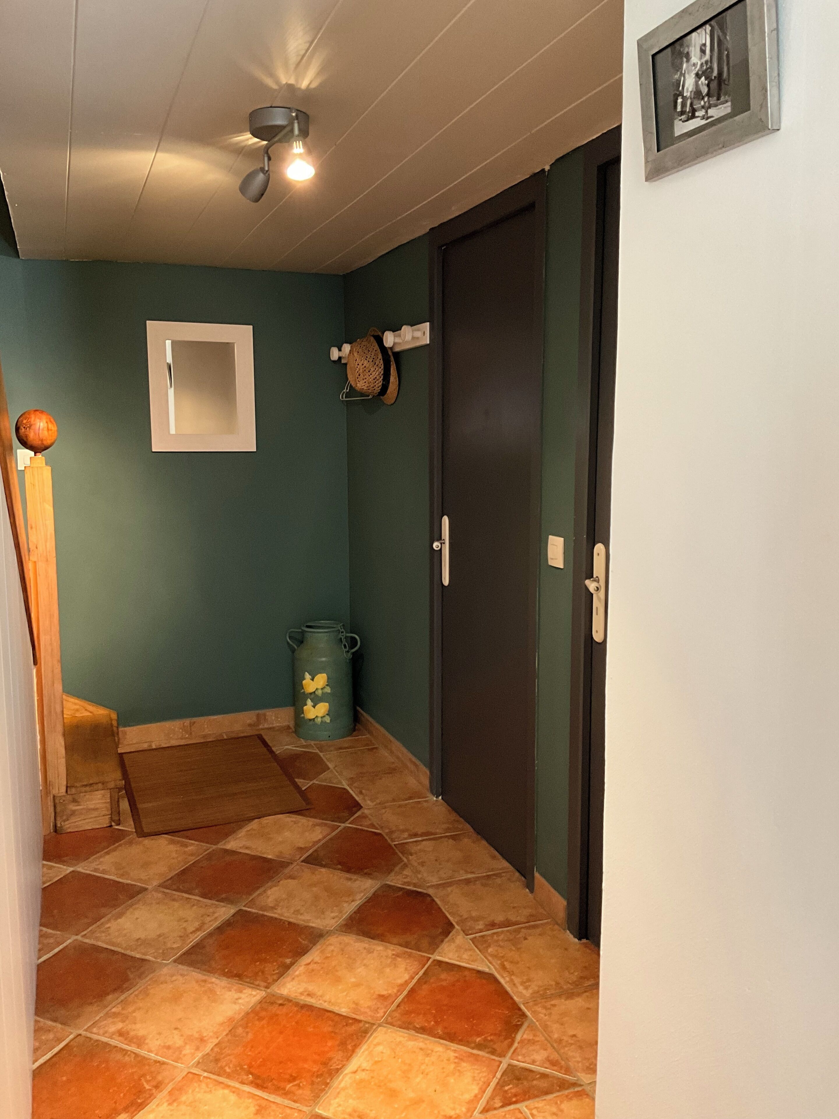 Un passadís amb terra de rajola, un ventilador al sostre, una porta amb mànec i un quadre al mur.