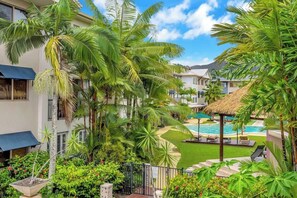 Een resort met een zwembad, palmbomen en een gazebopje met rieten dak.