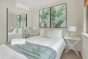 A hotel room with a bed, a mirror, two bedside tables with lamps, and artwork on the wall.