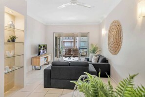 A modern living room with a sofa, a TV, a glass cabinet, and a balcony with outdoor furniture.