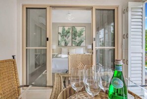 Una stanza con un letto, una poltrona in vimini, un tavolo con bicchieri da vino e una bottiglia.