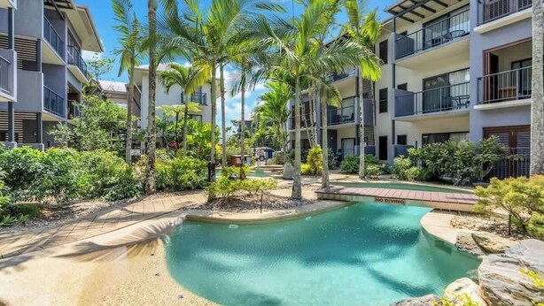 A pool surrounded by palm trees and a building with balconies.