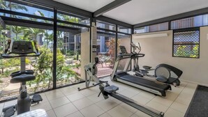 A gym with exercise equipment, large windows, and a view of palm trees.