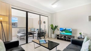 Una sala de estar moderna con un ventanal que da a un balcón, un televisor de pantalla plana y una mesa de centro.