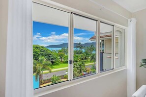 A room with a large sliding glass window offering a view of a lush landscape with greenery and a distant mountain range.