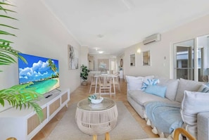 Una sala de estar con televisor, sofá, mesa de centro y comedor.