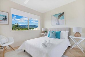 A hotel room with a bed, two bedside tables, a chair, a large window with a view, and artwork on the walls.