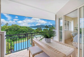 Varanda com vista para uma piscina e montanhas, uma mesa com uma planta e uma porta de correr de vidro.