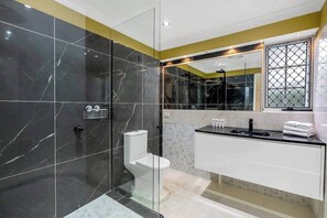 A modern bathroom with a glass-enclosed shower, a white toilet, and a black sink with a mirror above it.