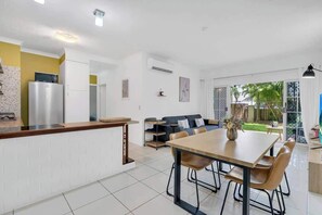 A modern kitchen with a dining area, white walls, and a view of the outdoors.